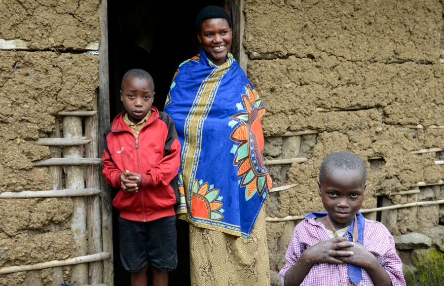 Eine junge Mutter steht mit zwei Kindern im Türrahmen eines Lehmhauses in Ruanda