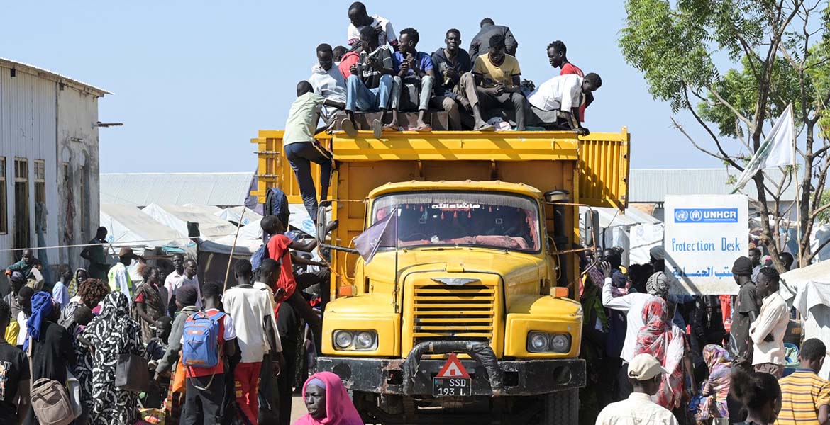 Geflüchtete in einem Flüchtlingslager in Renk im Südsudan. Sie sitzen teis auf einem riesigen gelben LKW, andere bewegen sich um das Fahrzeug herum.