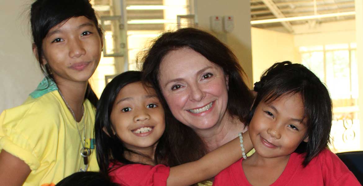 Uschi Dämmrich von Luttitz mit drei Kindern, von denen sie umarmt wird, auf den Philippinen.
