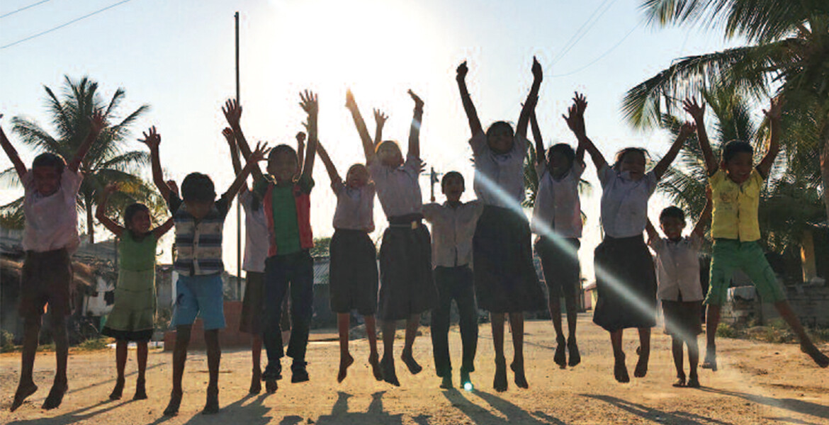 Kinder im Breads-Projekt in Bangalore springen freudig hoch und strecken ihre Arme in die Luft.