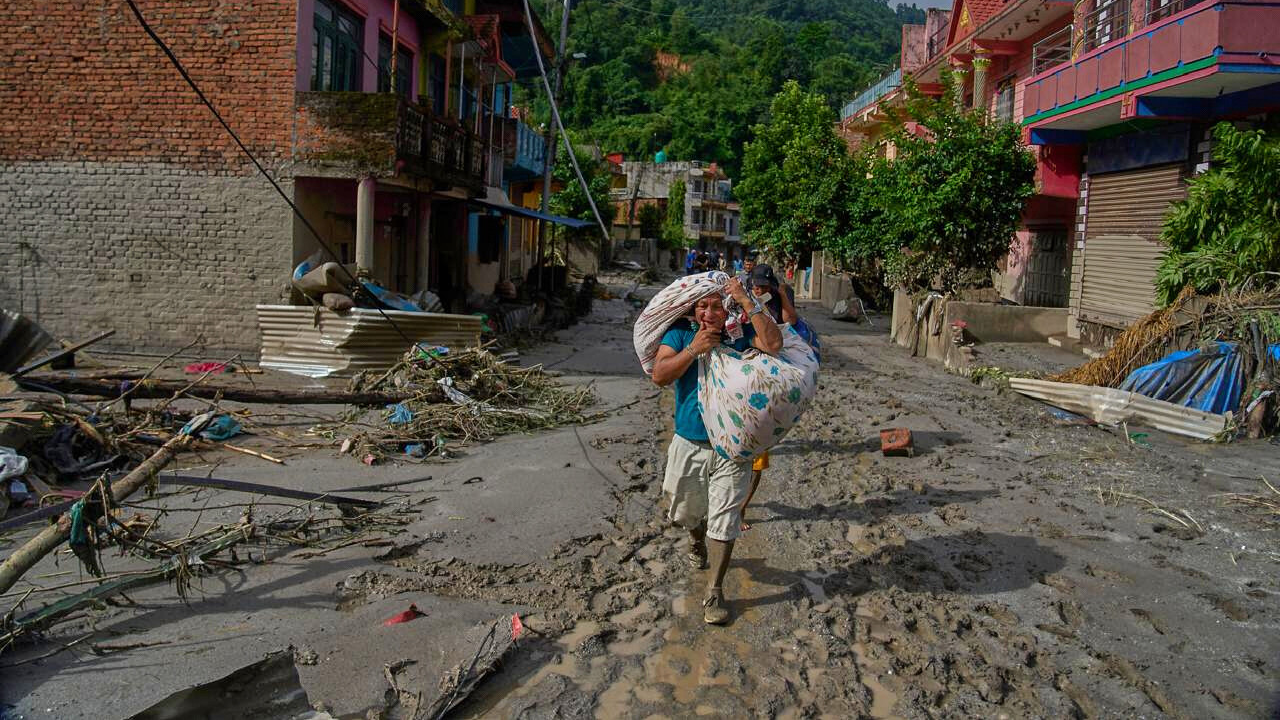 Ein Mann läuft auf von der Sturzflut in Nepal zerstörten Straße eines Dorfes der Kamera entgegen. Er trägt in Bündeln seine Habseligkeiten über den Schultern.