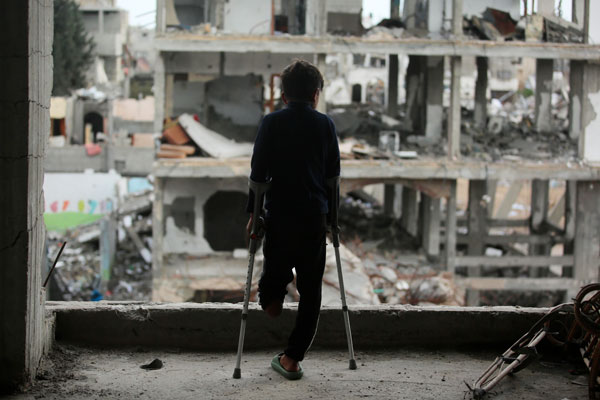 Ein Junge aus Gaza mit amputiertem linken Bein steht in einem kaputten Haus und blickt auf Ruinen