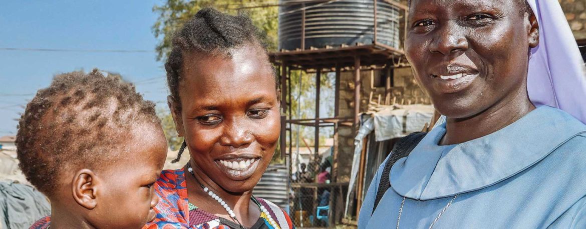 Afrikatag 2026: Eine Schwester aus Südsudan steht bei einer Frau, die ein Kind auf dem Arm hält.