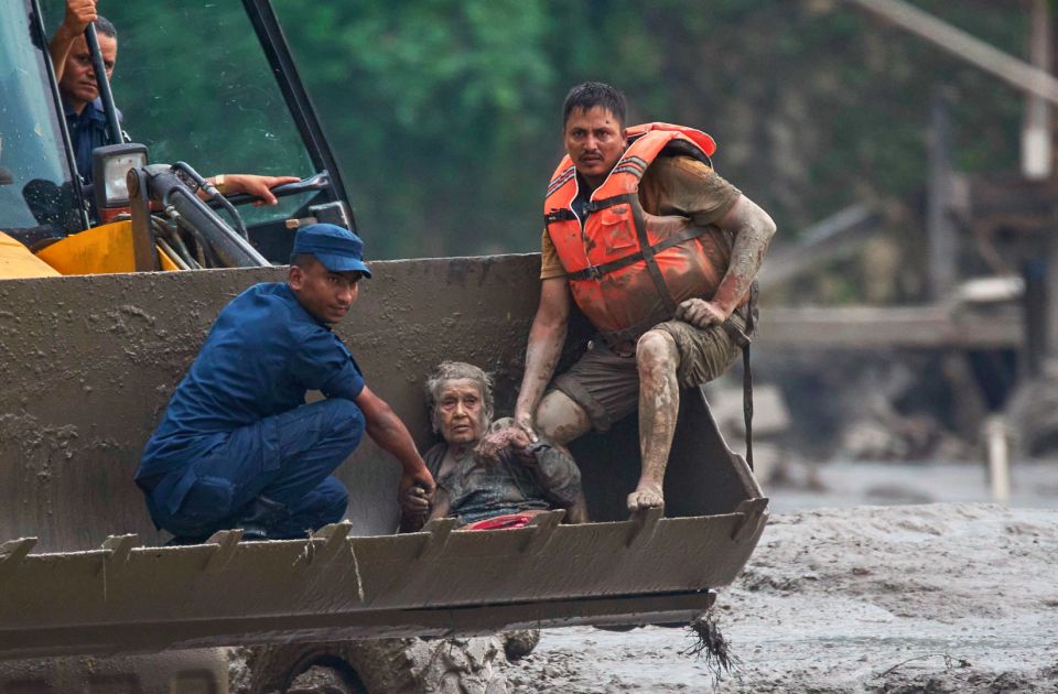 Eine alte Frau sitzt erschöpft mit zwei Helfern in einer Baggerschaufel. Sie wurde zuvor aus den Fluten in Nepal gerettet.