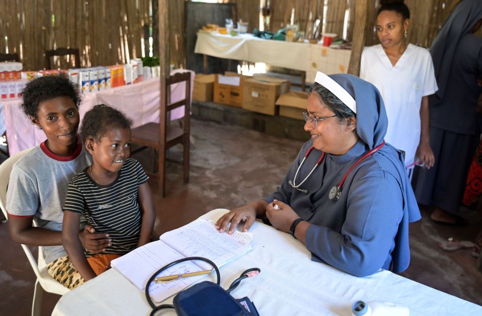 Blick in eine mobile Klinik auf Madagaskar: Sr. Jain Mary am Tisch mit ihrer jungen Patientin Mira, die auf dem Schoß ihrer Mutter sitzt