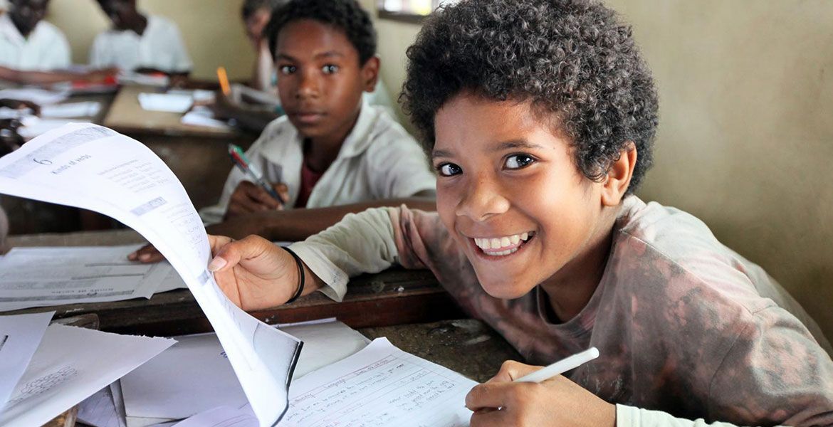 Ein Junge aus Papua-Neuguinea sitzt in der Schule und blickt lächelnd von den Unterlagen hoch