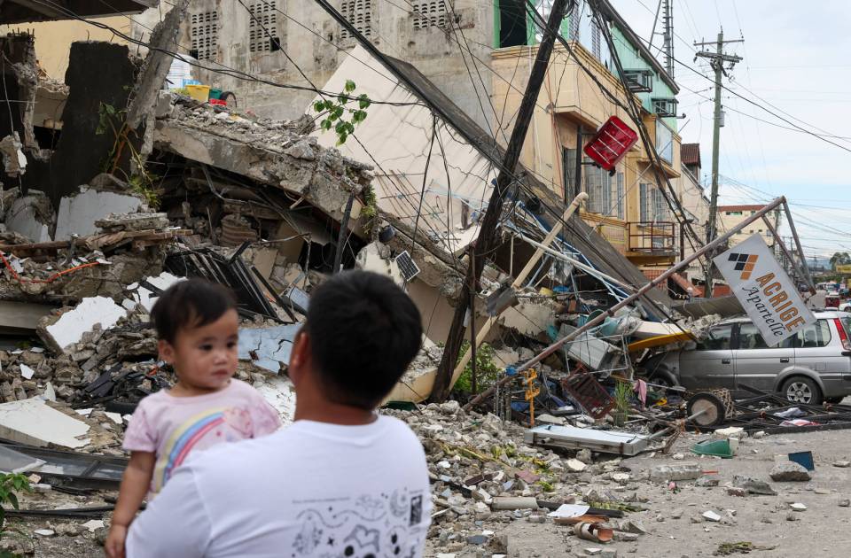 Ein Mann mit einem Kind auf dem Arm steht vor einem vom Erdbeben völlig zerstörten Gebäude in Bogo City in der Region Cebu auf den Philippinen