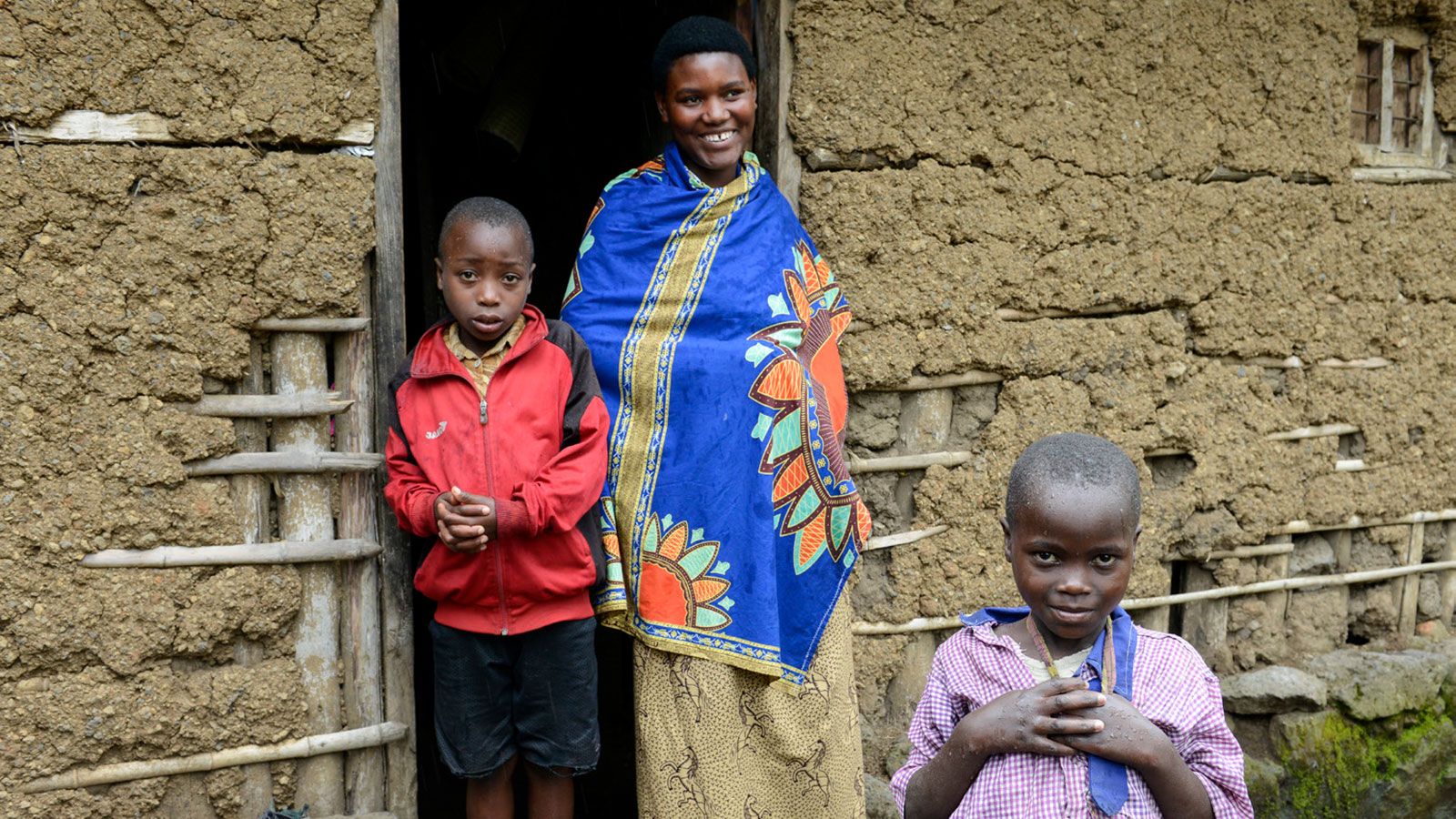 Eine junge Mutter steht mit zwei Kindern im Türrahmen eines Lehmhauses in Ruanda