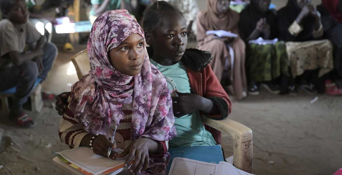 Zwei Kinder sitzen in Renk im Südsudan in einer provisorischen Schule mit ihren Schulheften auf dem Schoß auf einem Plastikstuhl.