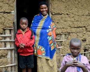 Eine junge Mutter steht mit zwei Kindern im Türrahmen eines Lehmhauses in Ruanda