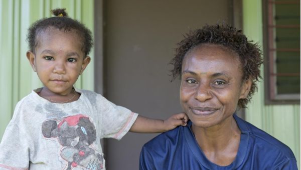 Vero James und ihre Tochter sitzen vor einem Frauenhaus in Papua-Neuguinea und lächeln hoffnungsvoll in die Kamera