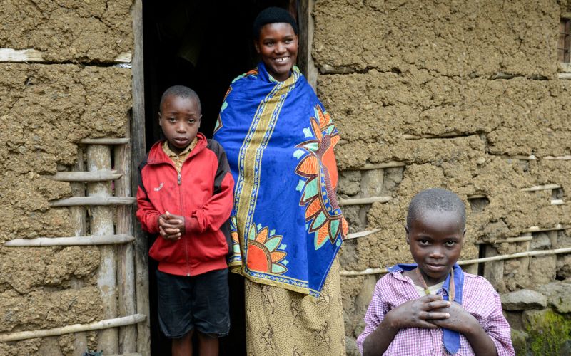 Eine junge Mutter steht mit zwei Kindern im Türrahmen eines Lehmhauses in Ruanda